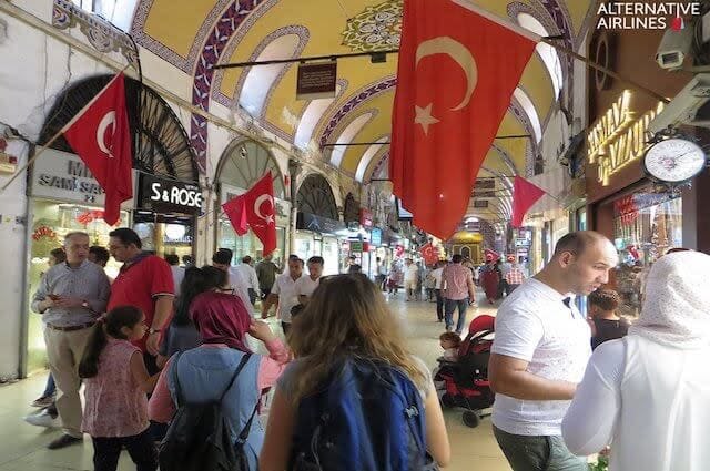 Bustling market in Istanbul with red Turkish flags flying above the promenade of shops and people milling about