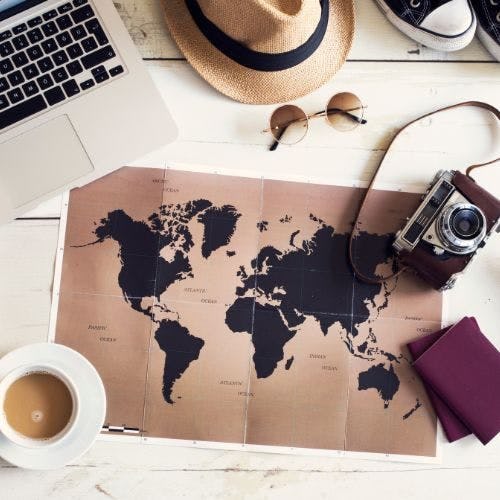 A map on a table with a laptop, coffee, camera, passports and sunglasses