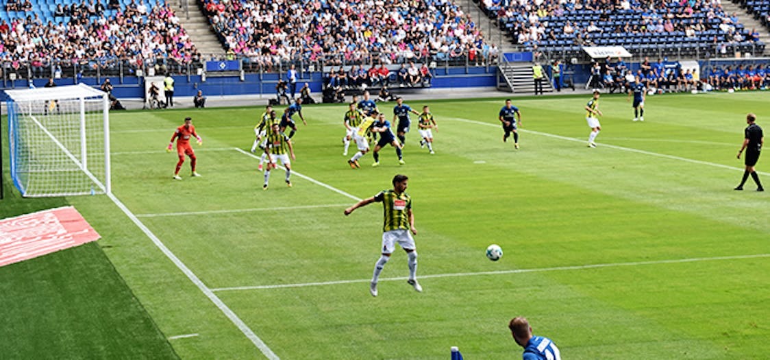 Football match being played on a grass pitch with crowds of fans sitting around the pitch