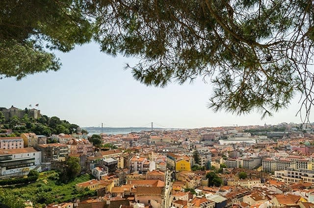 A view of the city of Lisbon in sunshine with red tiled roofs and green trees