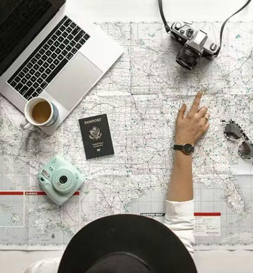 Picture of a map, passport, cameras, laptop and a person making travel plans