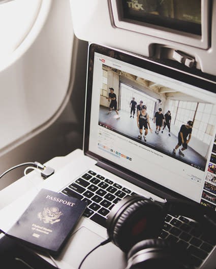 A laptop, headphones and US passport on an airplane tray table under the seat back TV screen 