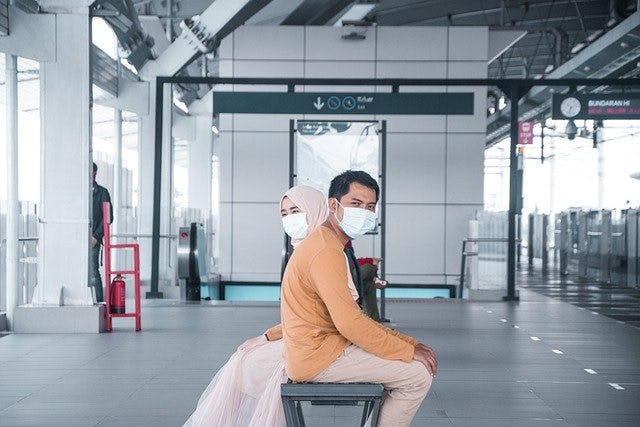 2 People Sitting at Airport/Station with Masks
